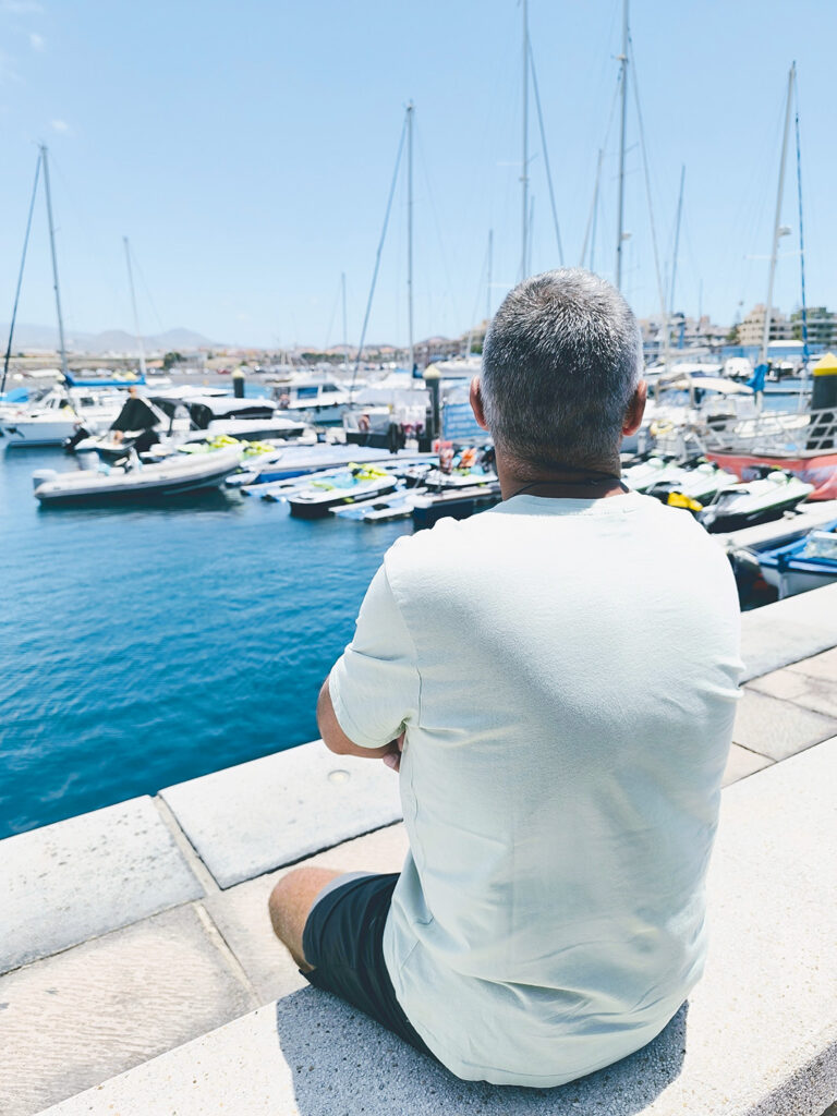 Man som sitter och tittar på båtar på våren i en hamn i Spanien 