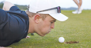 Ung golfare blåser på golfboll.